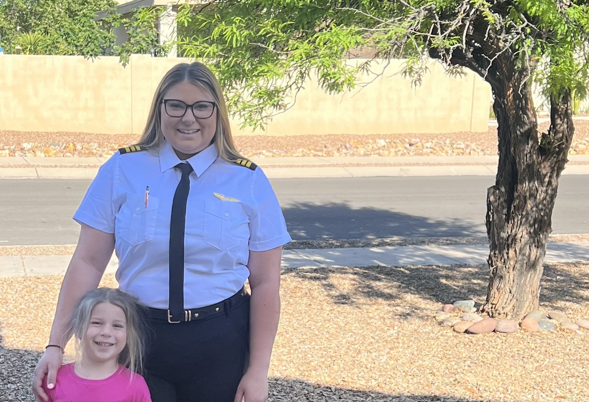 Sarah Tanis standing in her pilot uniform with her daughter. 